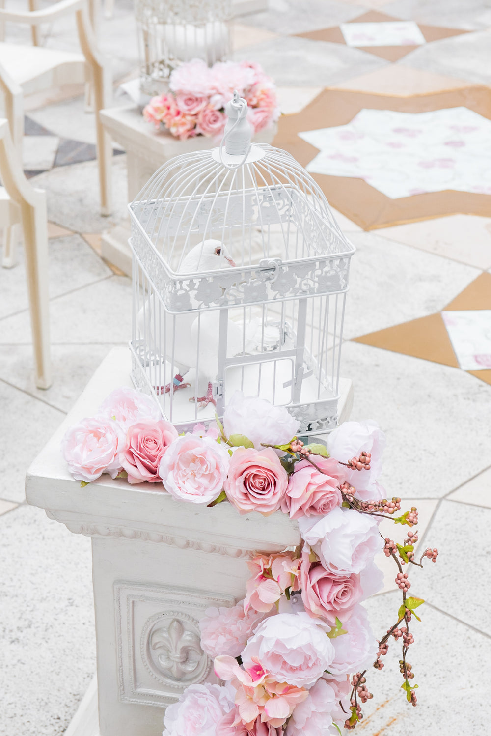 A white dove in a decorative cage surrounded by pink flowers