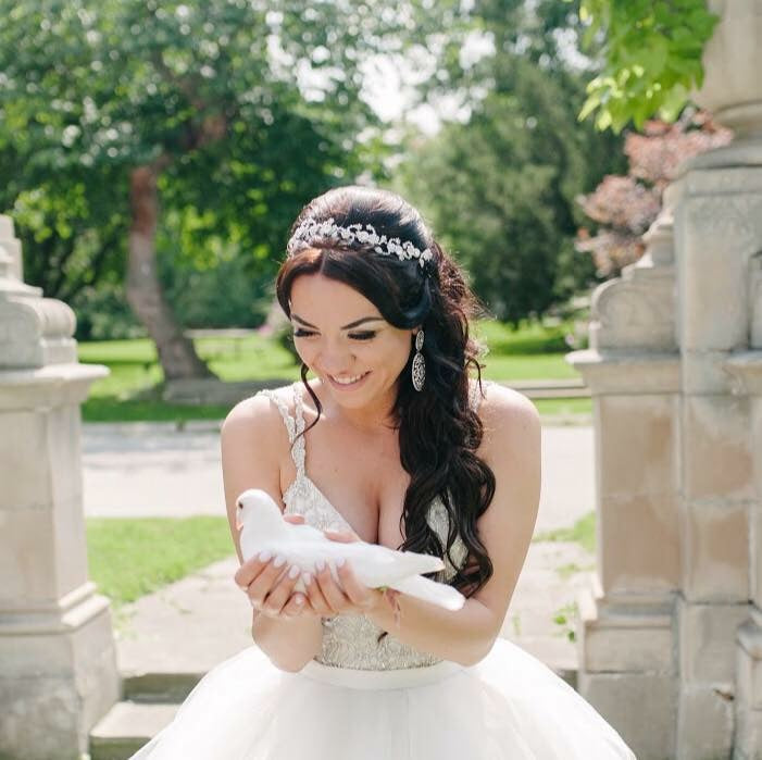 A bride smiling as she holds a white dove in a garden